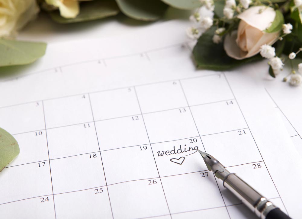 Wedding calendar with pen writing text on planning date on background with roses
