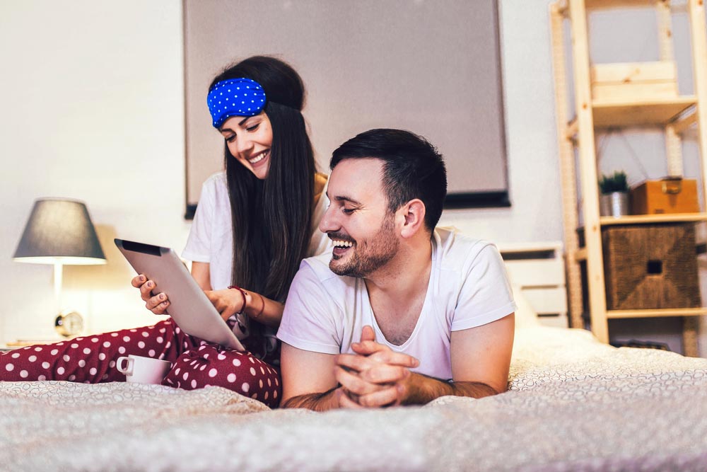 Smiling relaxed young couple using digital tablet in bed at home