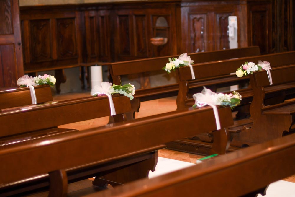 Elegant church pews adorned with white and pink flowers and delicate ribbons, creating a romantic and festive atmosphere for a wedding ceremony.