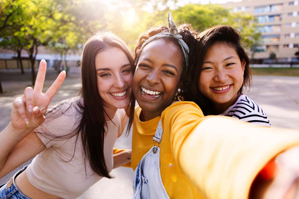 Female friendship concept with three diverse young women taking selfie outdoor. Happy millennial ladies having fun together on summer vacation.
